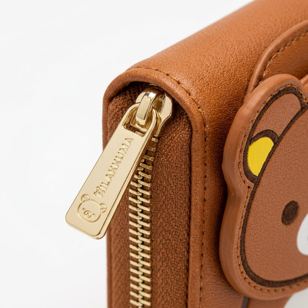 Close-up of gold-tone zipper pull and textured faux-leather stitching on Rilakkuma wallet